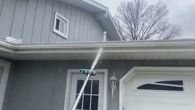 Gutter and soffit line of a two-story home being rinsed with a pole-fed spray
