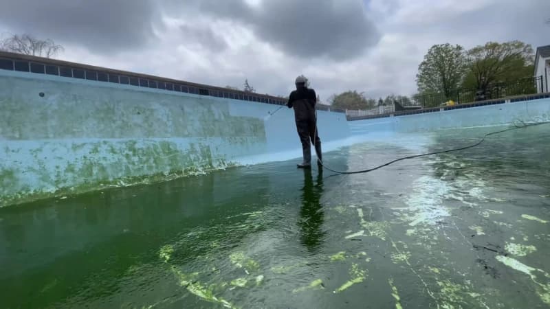 Technician rinsing algae from the floor of a large drained swimming pool