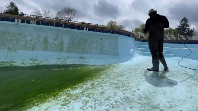 Technician washing the algae line along the wall of a drained swimming pool