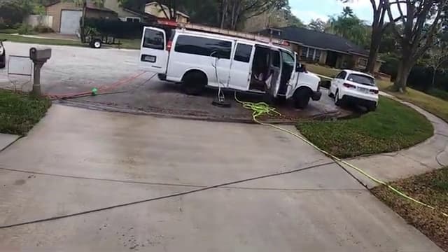Service van parked on a residential driveway with pressure washing hoses run out to the job
