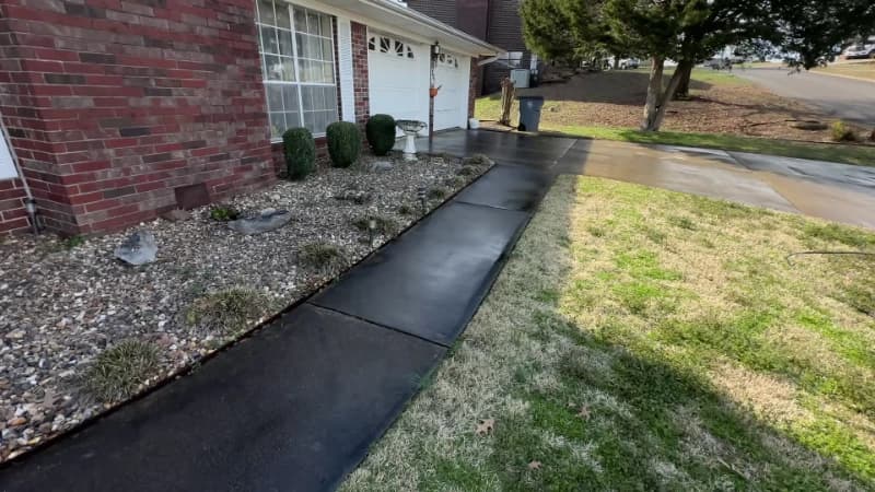 Concrete walkway beside a brick home darkened by organic growth before pressure washing