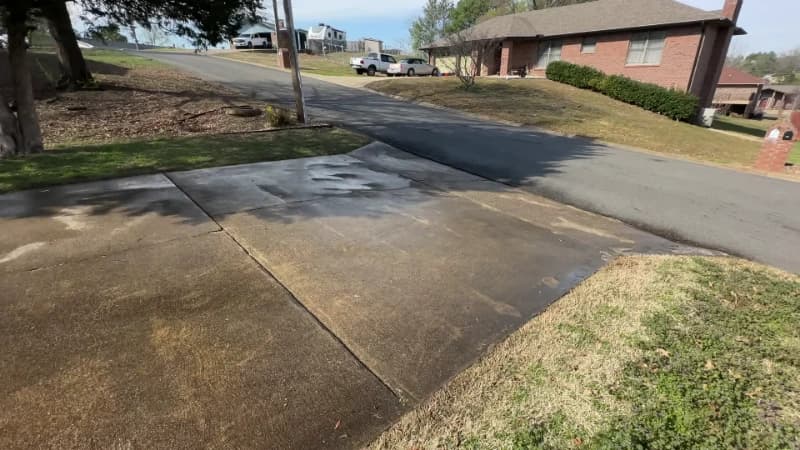 Concrete driveway meeting the street, stained with road film and traffic marks before cleaning