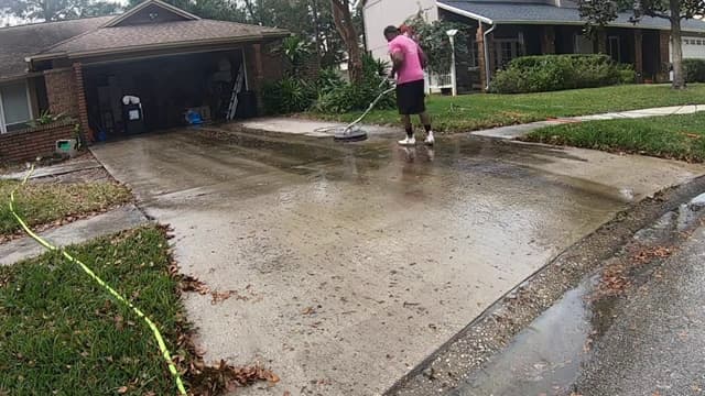 Technician running a surface cleaner over a stained residential concrete driveway