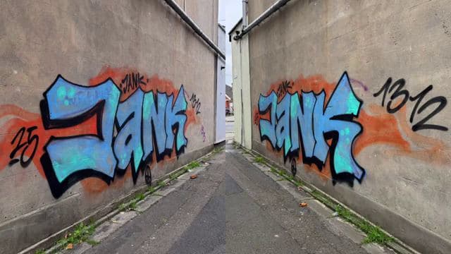 Blue and orange spray-painted graffiti covering both concrete walls of a narrow alley
