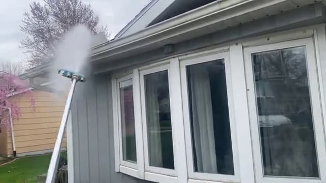 Pole-mounted brush washing the siding and gutter line above a bay window