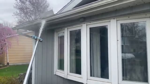 Pole-fed spray reaching the upper siding and gutter line of a home from the ground