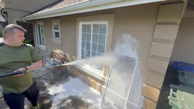 Technician rinsing a removed window screen propped against the stucco wall of a home