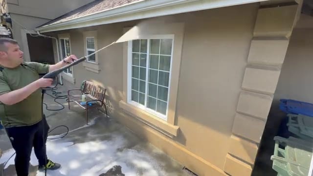 Technician soft washing the stucco wall of a home with a low-pressure wand